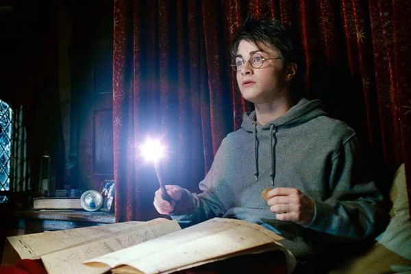 FOTO COLORIDA DE HARRY POTTER SENTADO COM VARINHA ACESA SOBRE PAPEL - METRÓPOLES