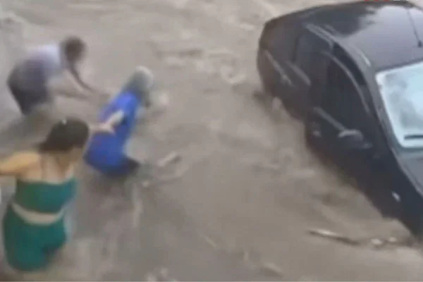 Imagem colorida de grupo resgatando pessoas de carro preso em enxurrada - Metrópoles