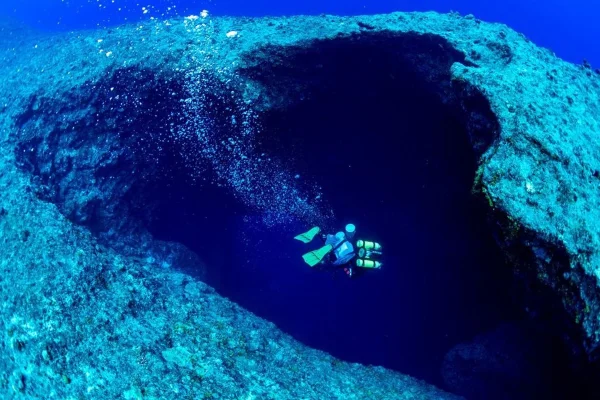 Foto colorida de expedição feita no oceano pacífico, com mergulhador entrando em um buraco que parece super profundo e escuro - Metrópoles.