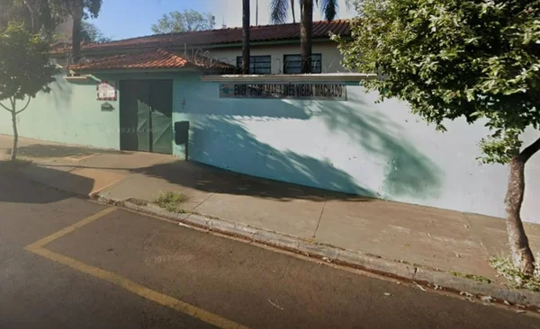 Imagem colorida mostra a fachada da escola Professora Maria Inês Vieira Machado, em Ribeirão Preto. O local tem uma árvore na calçada, muros azuis claros e portão verde - Metrópoles