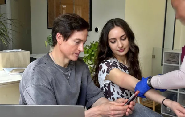 Foto colorida de Bryan Johnson e Kate Tolo durante coleta de sangue