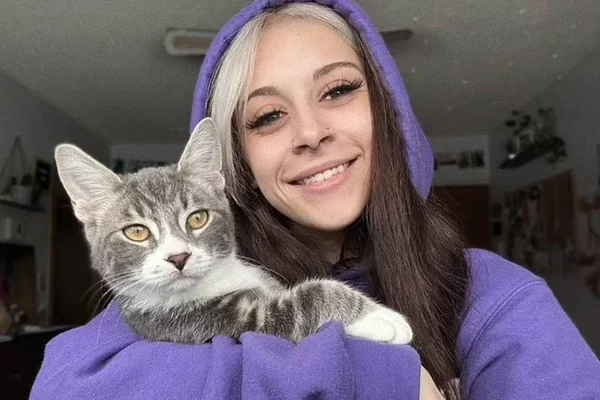 Foto de jovem de casaco roxo abraçada com gato cinza - Metrópoles