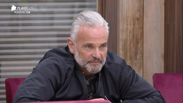 Foto de Mateus Carrieri. O ator tem cabelo e barba branca e está usando um casaco preto - Metrópoles
