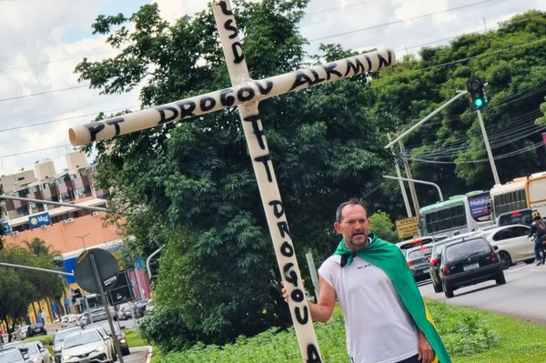 Imagem colorida de bolsonarista se manifestando na W3 Norte com cruz