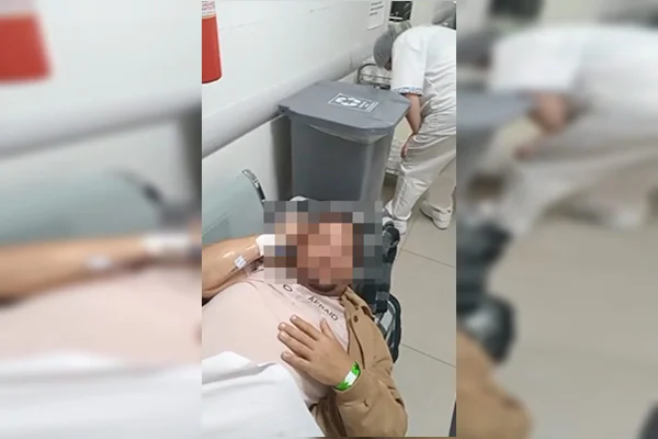 Foto colorida de homem deitado em banco de ferro em meio a corredor