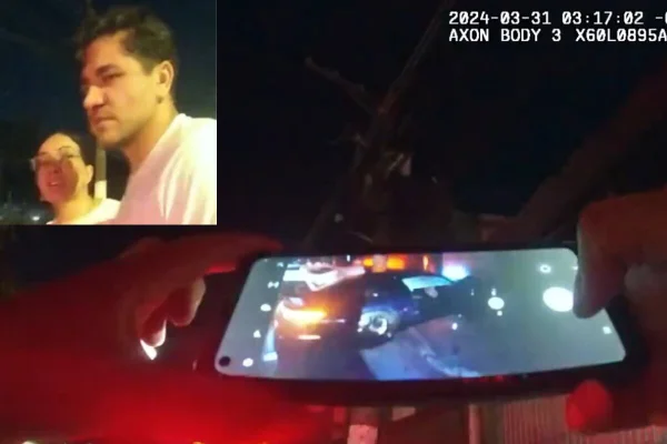 Imagem colorida de perspectiva de câmera corporal de duas mãos segurando celular que fotografa porsche acidentado - Metrópoles