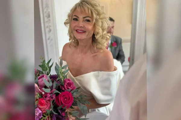 Foto colorida de mulher com vestido de noiva segurando um buquê nas cores rosa e roxo - Metrópoles.