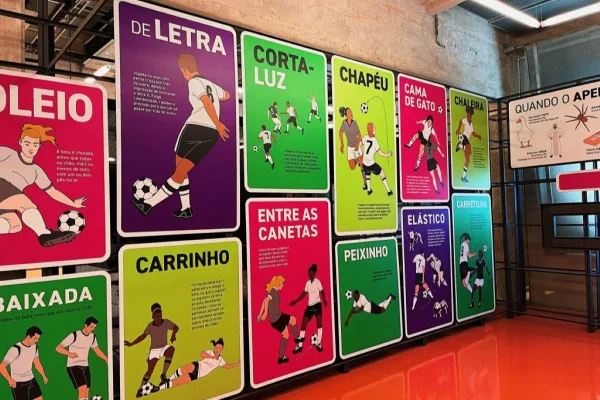 Parede com cartazes coloridos com ilustrações mostrando passes do futebol como letra, carrinho e corta-luz - Metrópoles