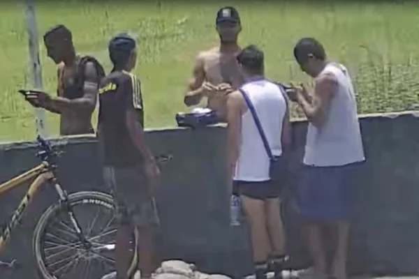 Foto colorida de traficantes comercializando drogas em frente à campo de futebol, em Cubatão, litoral sul de São Paulo.