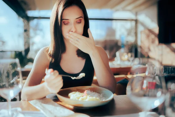Foto mostra mulher combrindo a boca como se buscasse disfarçar um arroto ou se estivesse comendo uma comida ruim - arrotar - metrópoles