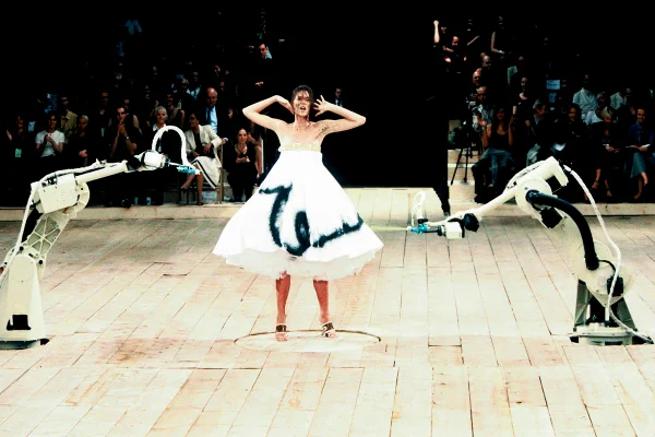 Na passarela da marca Alexander McQueen, modelo usa vestido branco que é pintado por máquinas com tinta - Metrópoles