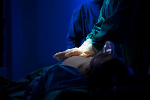 Imagem mostra close das mãos de uma pessoa de luvas fazendo massagem cardíaca em paciente deitado - Metrópoles