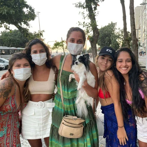 Cinco mulheres enfileiradas, em trajes de banho, com uma cachorrinha ao centro