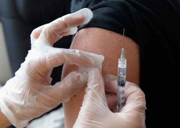 Mãos com luvas médicas seguram seringa de vacina e aplicam curativo em braço