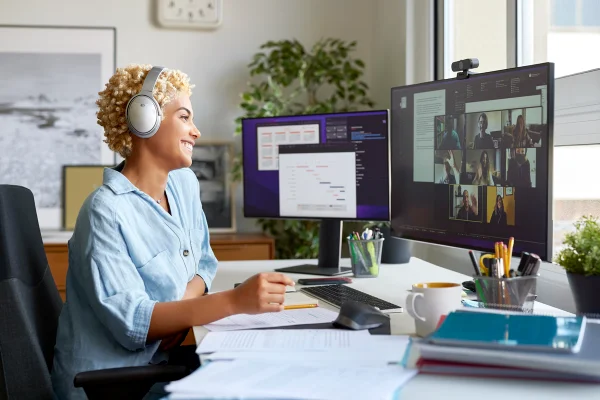 Foto colorida de mulher sorrindo em frente ao computador emquando participa de uma reunião online - Metrópoles.