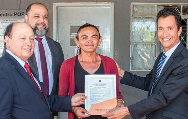 Imagem colorida de mulher trans recebendo certidão de nascimento