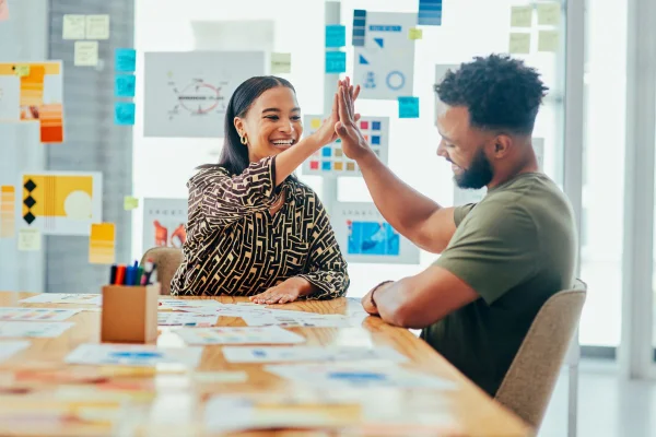 Dois jovens designers dando um ao outro um high five enquanto trabalham juntos em um escritório