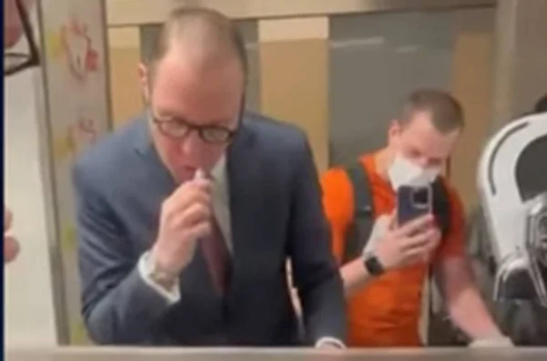 Imagem colorida de Zanin escovando os dentes em aeroporto enquanto é filmado por um homem de camiseta laranjada - Metrópoles