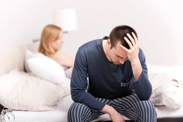 Homem chateado sentado na cama com mulher nas costas. Conceito de problemas sexuais. Metrópoles