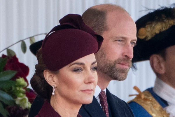 Foto colorida de mulher maquiada, com chapéu na cor vinho, ao lado de homem de barba e com terno - Metrópoles