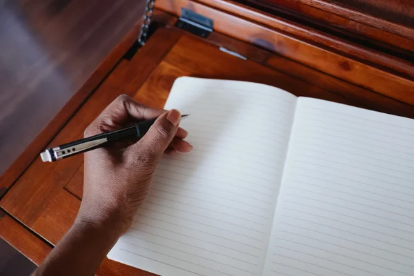 Foto colorida de pessoa se preparando para escrever em caderno branco - Metrópoles