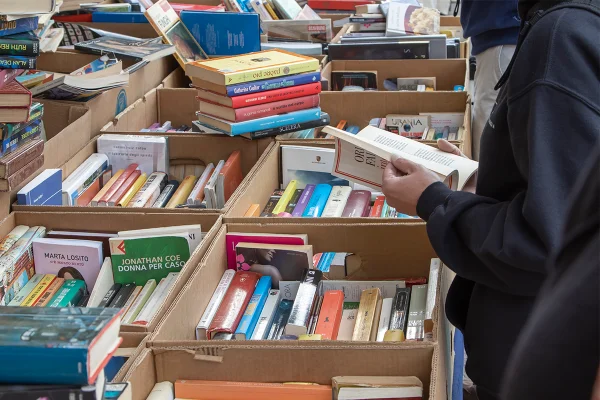 Livros em estante, com pessoa lendo uma obra. Livros estão dentro de caixas de papelão - Metrópoles