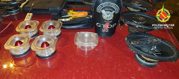 Caixas de som automotivo em cima de capô vermelho, com logo da PM acima