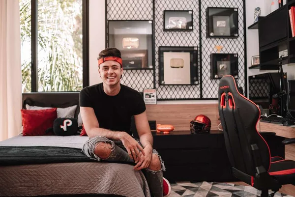O influenciador digital Enaldinho esta sentado numa cama sorrindo para a foto - Metropoles