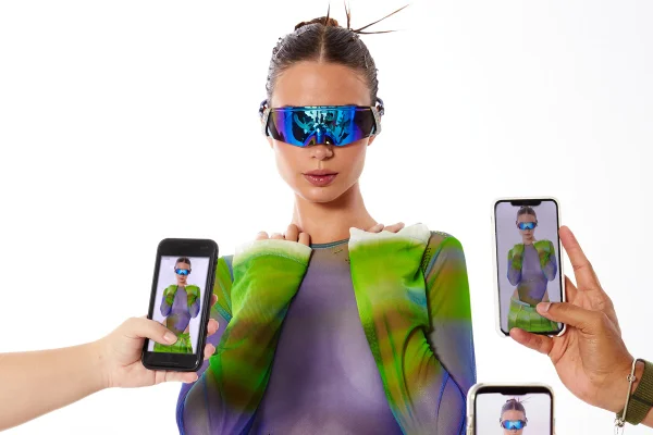 Com blusa de estampa psicodélica e óculos futurista, modelo posa para vários celulares - Metrópoles