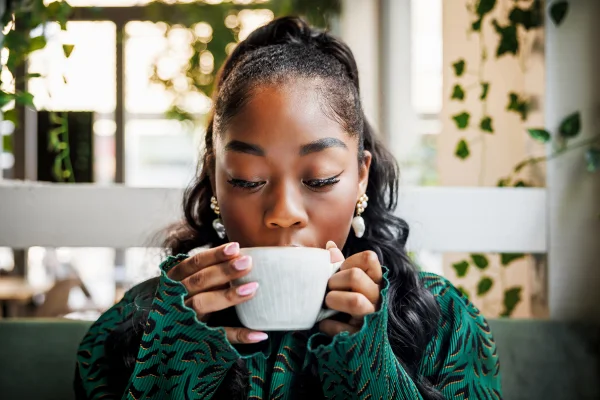 Uma jovem se delicia com o aroma do seu café, fechando os olhos para saborear o momento em um ambiente arborizado de cafeteria. bebida Caneca xíacara café chá