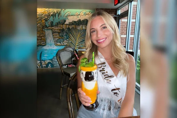 Foto de Kelsi Baldwin, uma mulher branca e loira, sorrindo para a foto e segurando uma bebida - Metrópoles