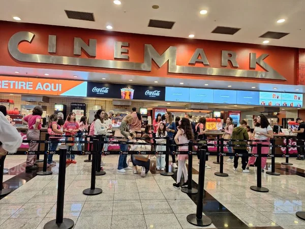 Imagem colorida mostra pessoas vestidas de rosa fazendo fila para comprar pipoca. Placa mostra nome "Cinemark" - Metrópoles