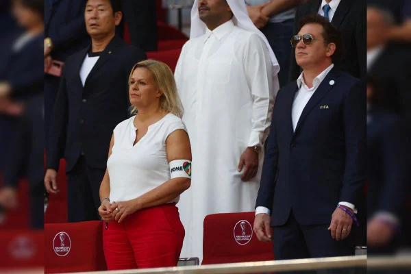 Imagem colorida mostra ministra da Alemanha, vestida de calça vermelha e camisa branca, com braçadeira em apoio à diversidade - Metrópoles