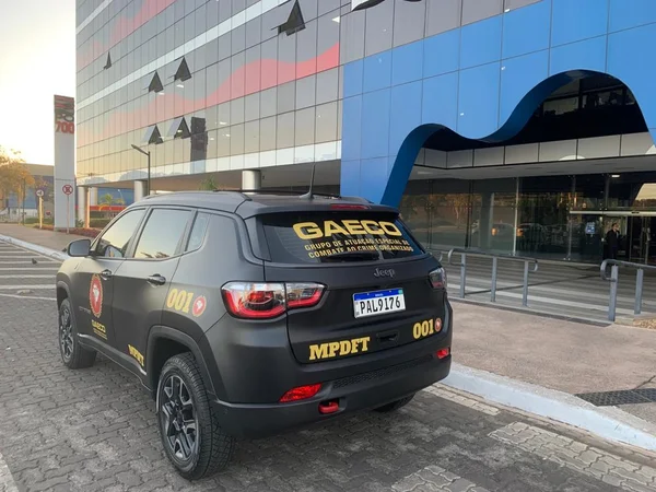 Carro preto da polícia civil em frente a um prédio com detalhes azuis e vermelhos