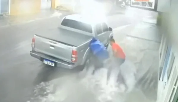 Imagem colorida mostra comerciante indo socorrer mulher que caiu e foi arrastada pela correnteza causada por uma forte chuva - Metrópoles