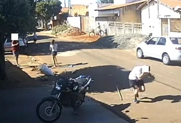 Vídeo de câmeras de segurança mostra homem (a direita) correndo de atirador, seu vizinho (a esquerda), após ser baleado na cabeça, no Mato Grosso do Sul. Eles correm numa rua com casas, onde também é possível ver uma mulher e uma criança - Metrópoles