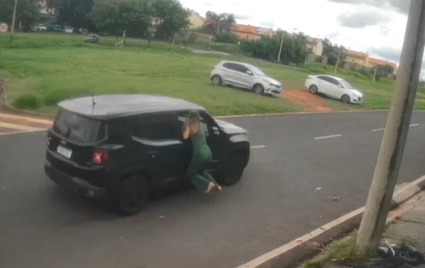 Imagem colorida mostra mulher pendurada na janela de um carro sendo arrastada por uma avenida - Metrópoles