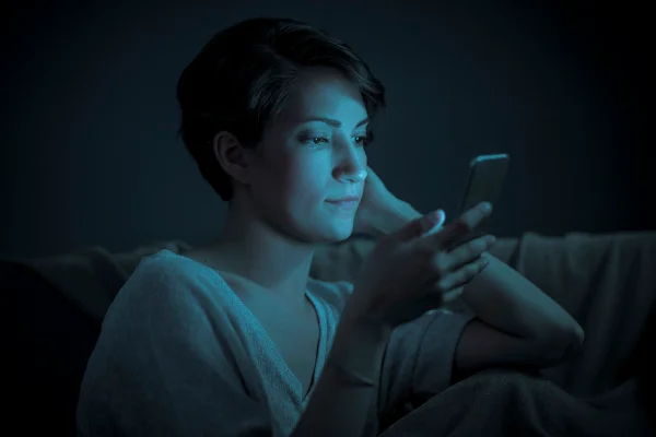 Imagem mostra uma mulher no escuro, iluminada pela luz azul do celular - Metrópoles