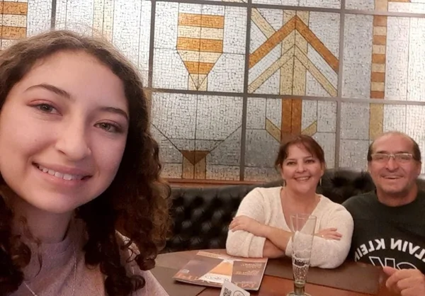 Família sorri para foto; menina à frente, em primeiro plano, e casal atrás, abraçado