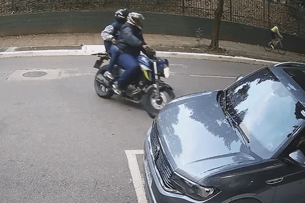 Imagem colorida de uma câmera de segurança mostra dois homens em uma motocicleta empunhando uma arma e dando a volta em uma rua antes de assaltar ciclista - Metrópoles