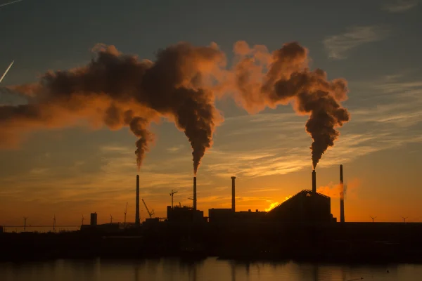 Foto colorida tirada ao pôr do sol que mostra tubos indústiais repelindo gases que provocam o efeito estuda e o aquecimento do planeta - Metrópoles.