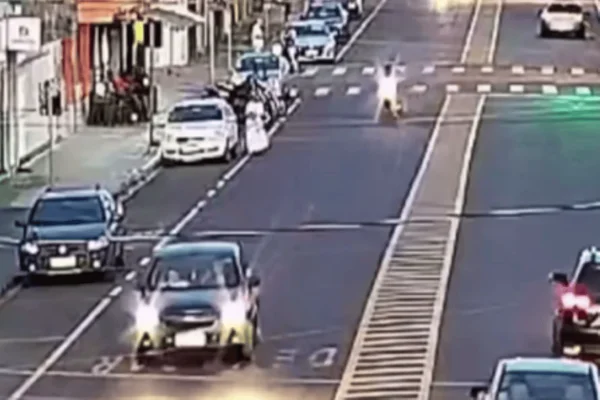 Imagem colorida de uma câmera de segurança mostra uma motocicleta avançando contra uma idosa de cadeira de rodas próxima ao meio-fio; motociclista - Metrópoles