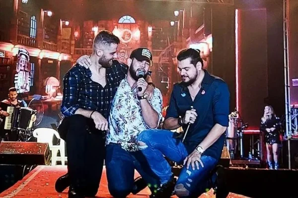 A imagem colorida mostra a dupla Zé Neto & Cristiano na ao lado de Tom Barboza em um palco