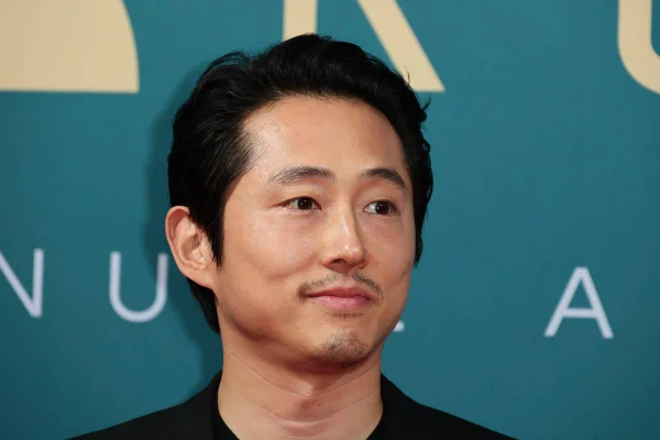 Ator Steven Yeun em frente a uma tela azul