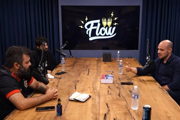 Homens sentados em mesa de madeira com quadro ao fundo escrito Flow