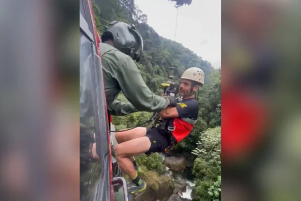 Imagem colorida mostra o repórter Lucas Martins sendo resgatado em helicóptero dos bombeiros - Metrópoles