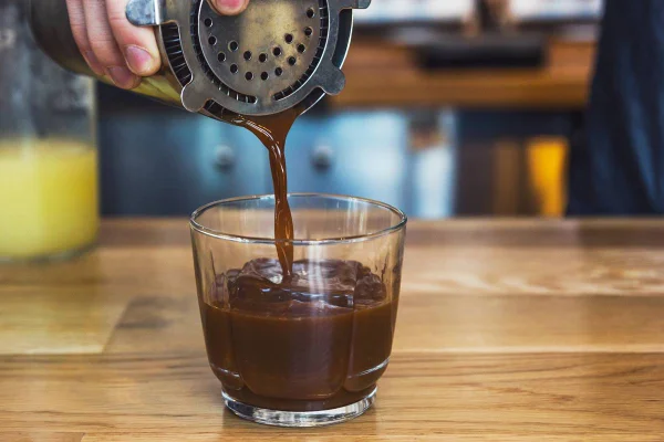 Mão derrama drinque feito com chocolate da coqueteleira em um copo