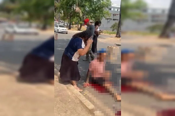 Foto colorida de homem no chão com perna coberta de sangue