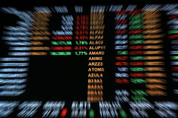 Imagem colorida desfocada do painel da Bolsa de Valores do Brasil, a B3, com os números que refletem o desempenho das ações negociadas