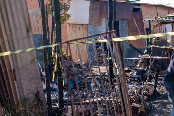 Imagem colorida de um barraco deteriorado por um incêndio, isolado por uma faixa preta e amarela